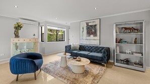 A modern living room with a blue sofa, a round coffee table, and a glass cabinet with decorative items. - Serene Lakefront Water side Villa with Private Pool  (Westlake)
