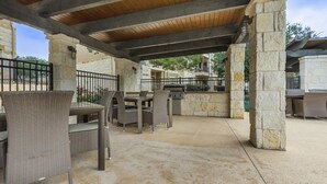Un espace extérieur aménagé en terrasse, avec des piliers en pierre, des meubles en osier et un barbecue.