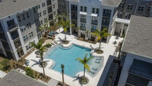 An aerial view of a residential building with a central swimming pool surrounded by palm trees and lounge chairs.