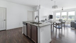 A modern kitchen with a central island, built-in dishwasher, and a dining area with a round table and chairs. - Landing | Modern 2BD, Clubhouse, Yoga Studio (Jacksonville)