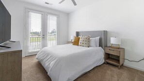 Une chambre à coucher comprenant un lit, des tables de chevet, un téléviseur et une porte coulissante donnant sur un balcon.