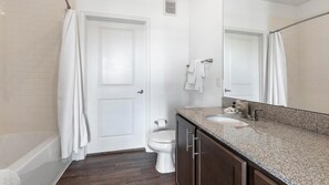 Une salle de bain avec des toilettes blanches, un lavabo doté d’un plan de travail en granit et un miroir au-dessus du lavabo.