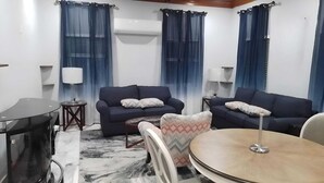 Een woonkamer met twee donkere banken, een ronde tafel, een gestreept fauteuil en een tv-meubel.