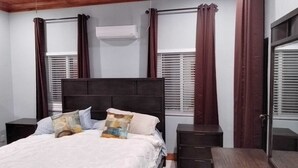 Een slaapkamer met een bed, twee nachtkastjes, een houten hoofdbord, een raam met zonwering en een airconditioning.