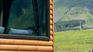 A log cabin with a large window, a view of a mountain range, and a grassy field. - Kazbegi Inn Cottages  (Kazbegi)