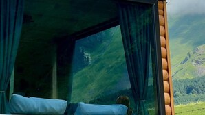 A room with a large window offering a view of a mountain range and lush green hills. - Kazbegi Inn Cottages  (Kazbegi)