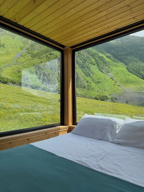 Un dormitorio con un ventanal que ofrece vistas a un valle verde y montañas.