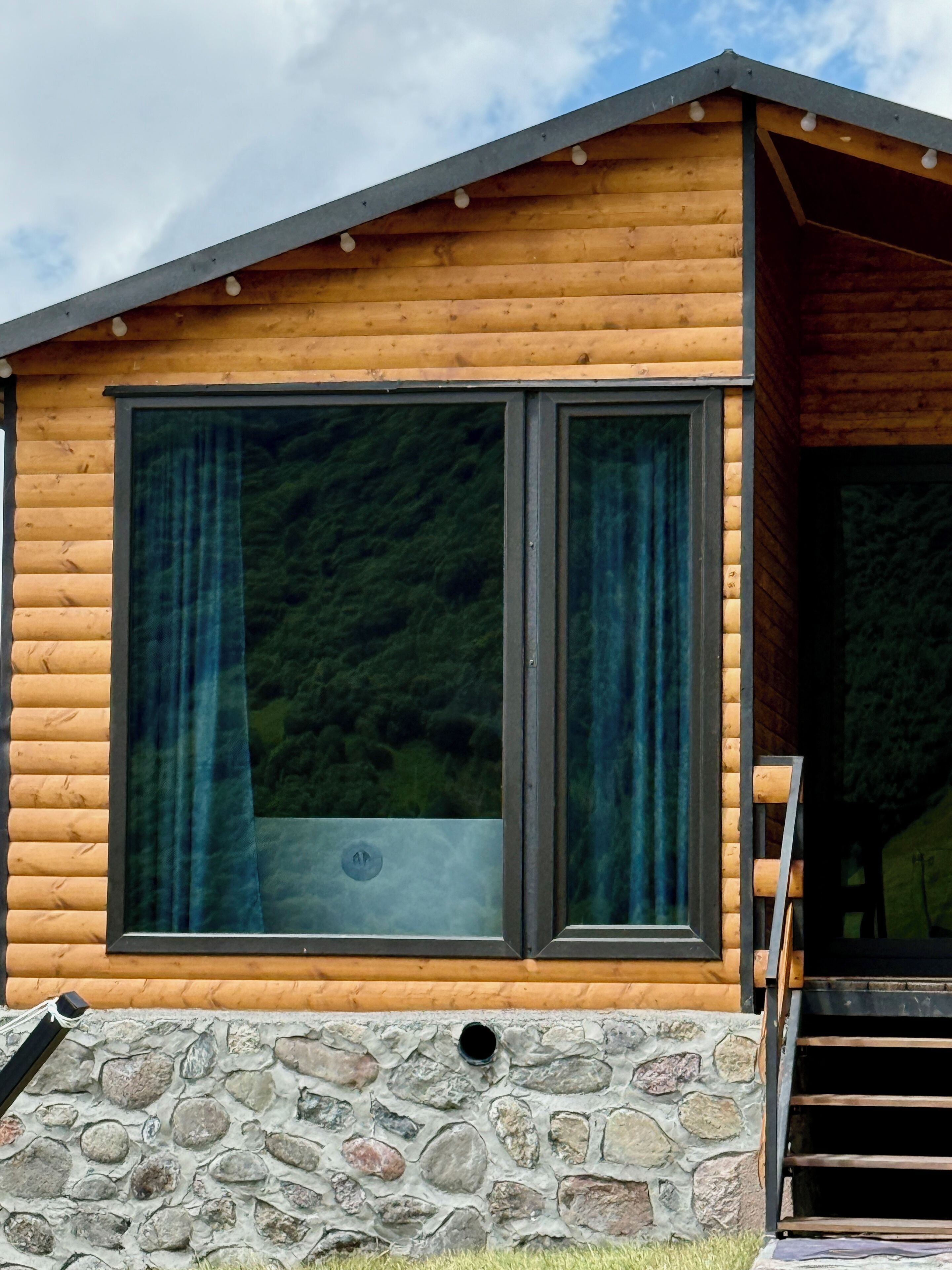 A wooden cabin with large windows and a stone foundation.