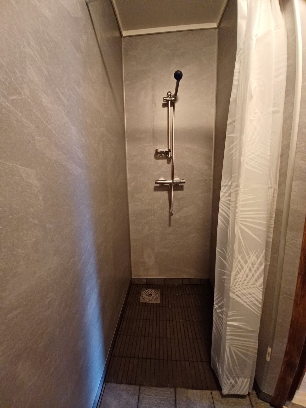 A small, tiled shower area with a handheld showerhead and a wall-mounted faucet.