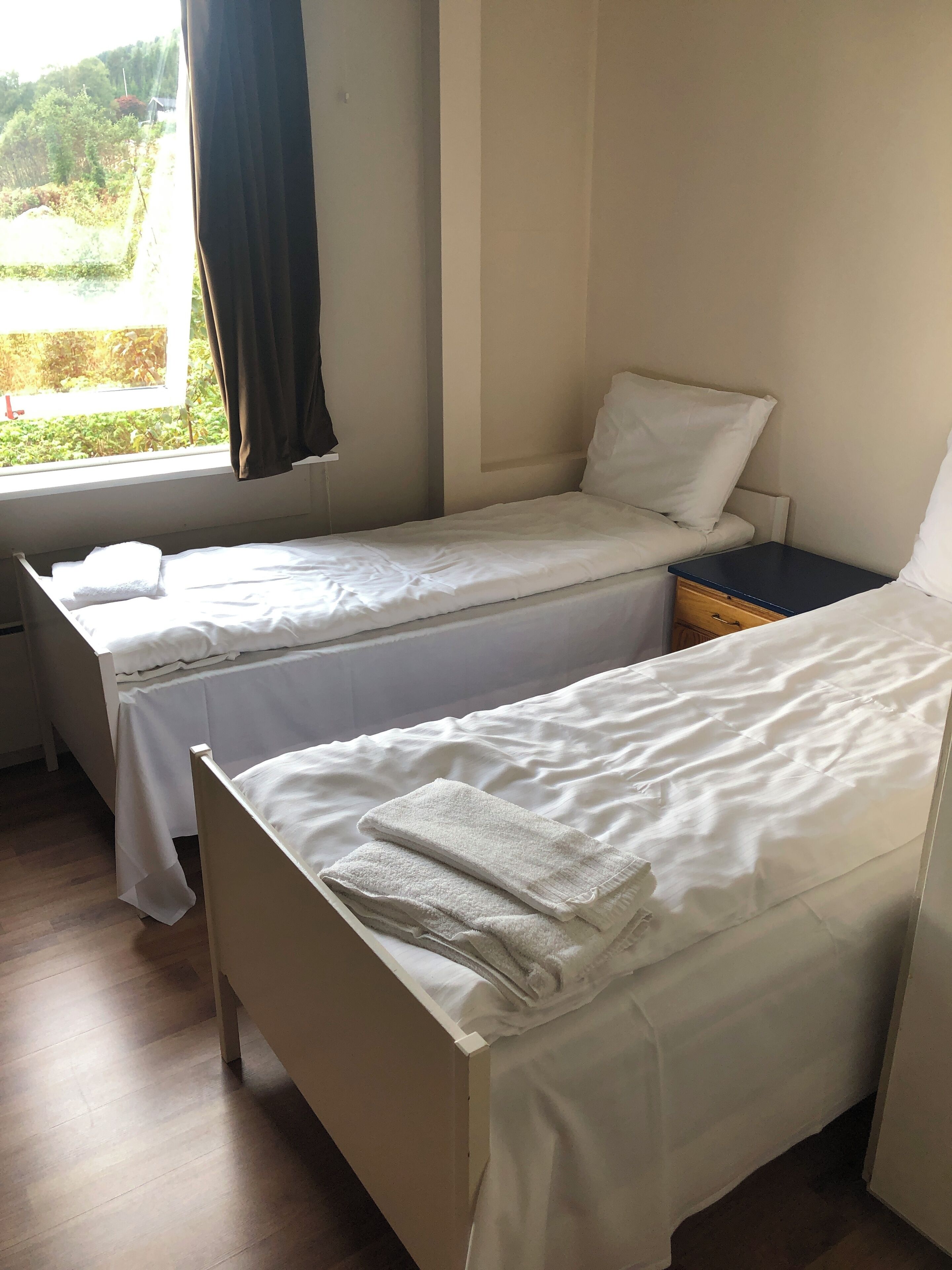 A room with two single beds, a small bedside table, and a window with curtains.