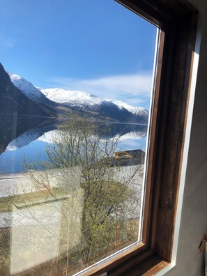 A window with a view of snow-capped mountains, a lake, and a road. - Jølster Lake View (Sunnfjord)