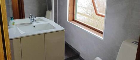 A bathroom with a white sink, mirror, and toilet. There is a window with a view of a mountain.