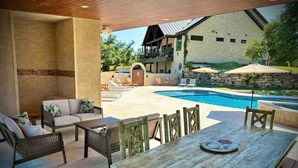 An outdoor patio with a pool, lounge chairs, and a wooden table. - The Family Retreat in Dripping Springs (Dripping Springs)