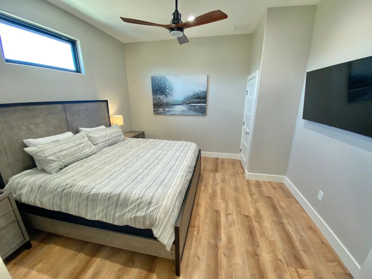 Ein Schlafzimmer mit Bett, Deckenventilator, Gemälde, Fernseher und Fenster.