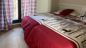 A bedroom with a sloped ceiling, a bed with a red and white patterned bedspread, plaid curtains, and a window with a view of trees.