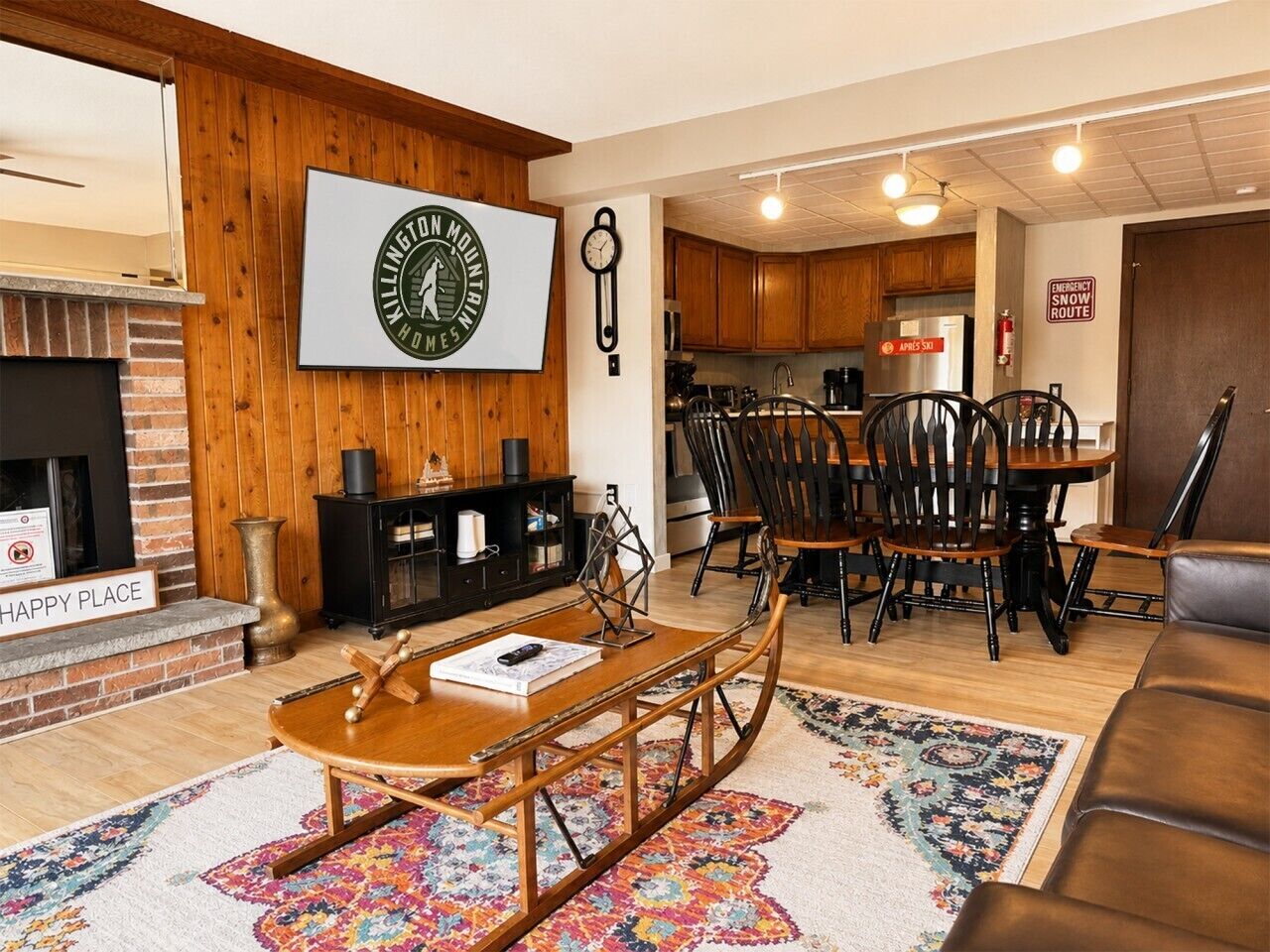 A cozy living room with a fireplace, a dining area with a wooden table and chairs, and a kitchen visible in the background.
