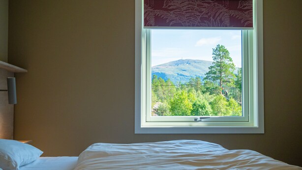 A bedroom with a bed, a window with a view of a mountain and trees. - KROKSTRAND FJELLPARK (Mo-I-Rana)