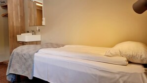 A small, neatly made bed with white linens and a gray blanket, a white bedside table with a mirror, and a wooden wardrobe in the background. - KROKSTRAND FJELLPARK (Mo-I-Rana)