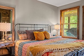Une chambre à coucher avec un lit, deux tables de chevet, une fenêtre avec des stores et un miroir au mur.