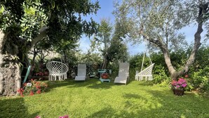 Un jardín con césped, sillas blancas y una hamaca.