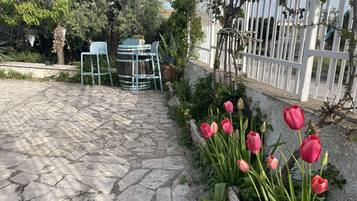 En uteplats med stenbeläggning, ett vitt staket, en pergola och en blomlåda med rosa tulpaner.