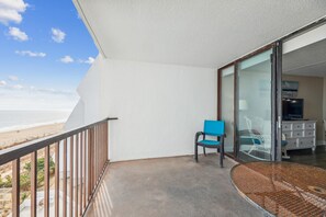 A balcony with a view of the beach, a chair, and a wicker table.