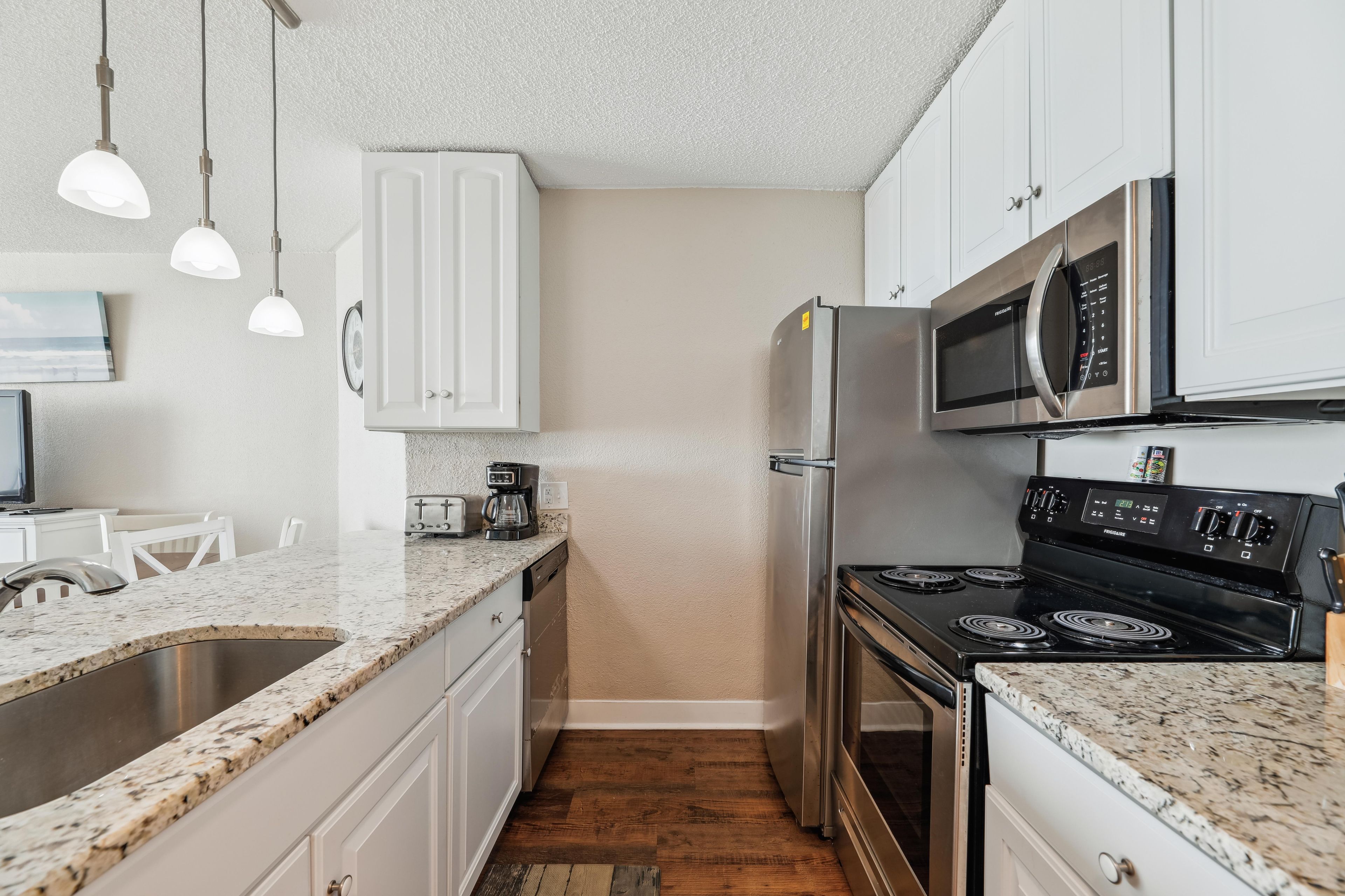 A kitchen with white cabinets, a stainless steel refrigerator, a microwave, a stove, and a coffee maker.