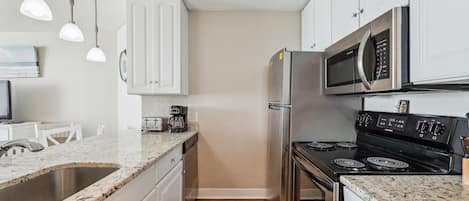 A kitchen with white cabinets, a stainless steel refrigerator, a microwave, a stove, and a coffee maker.