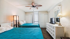 A hotel room with two beds, a ceiling fan, a television, and a dresser.