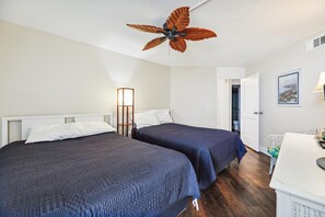 A hotel room with two beds, a desk, a ceiling fan, a lamp, and a door leading to a bathroom.