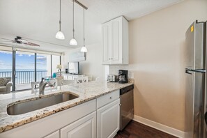 A modern kitchen with a large island, white cabinetry, a stainless steel refrigerator, and a view of the ocean.