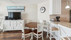 A compact living space with a dining area, kitchenette, and a mounted television.