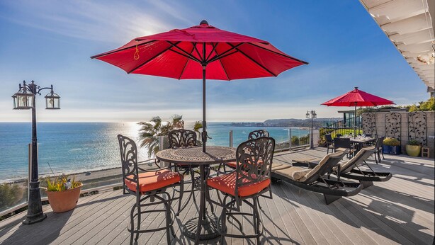 Une terrasse avec une table et des chaises, des parasols rouges et une vue sur l’océan.