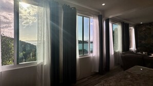 A room with large windows, a stone wall, and a seating area with a sofa and chairs. - Sunset Hideaway Suite - Oceanview/central to Cruz Bay  (St John)