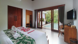 A bedroom with a bed, a desk, a TV, and a sliding glass door leading to a pool area. - The Sidemen Villas (Sidemen)