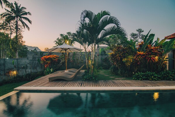 A poolside area with a wooden deck, lounge chairs, and an umbrella.