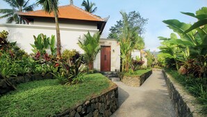 A pathway leading to a building with a stone wall on one side and lush greenery on the other. - The Sidemen Villas (Sidemen)