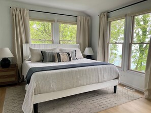 Un grand lit recouvert d’une couvre-lit à rayures, deux lampes de chevet et une vue sur les arbres par les fenêtres.