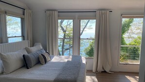 Quarto com cama grande, duas janelas e vista para o exterior.