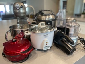 Una cocina con un procesador de alimentos rojo, una olla de cocción lenta blanca, una licuadora y una olla de acero inoxidable.