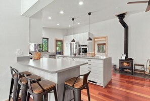 Uma cozinha moderna com uma ilha central, banquetas de bar e uma lareira a lenha.