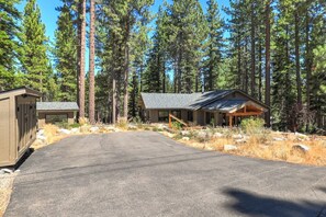 A two-story cabin with a covered porch, surrounded by tall pine trees.