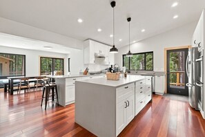 A modern kitchen with a central island, white cabinetry, and a dining area with wooden flooring.