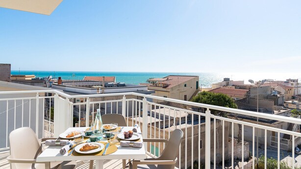 A balcony with a table set for two, overlooking a coastal cityscape.