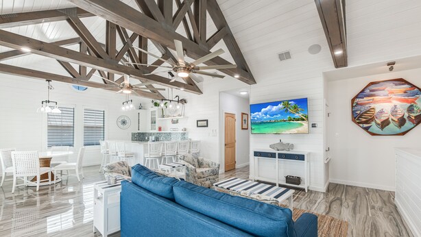 A spacious living room with a blue sofa, wooden ceiling beams, a TV, and a large painting of boats. - Over the top construction, beautifully decorated, close to everything Port A has (Port Aransas)
