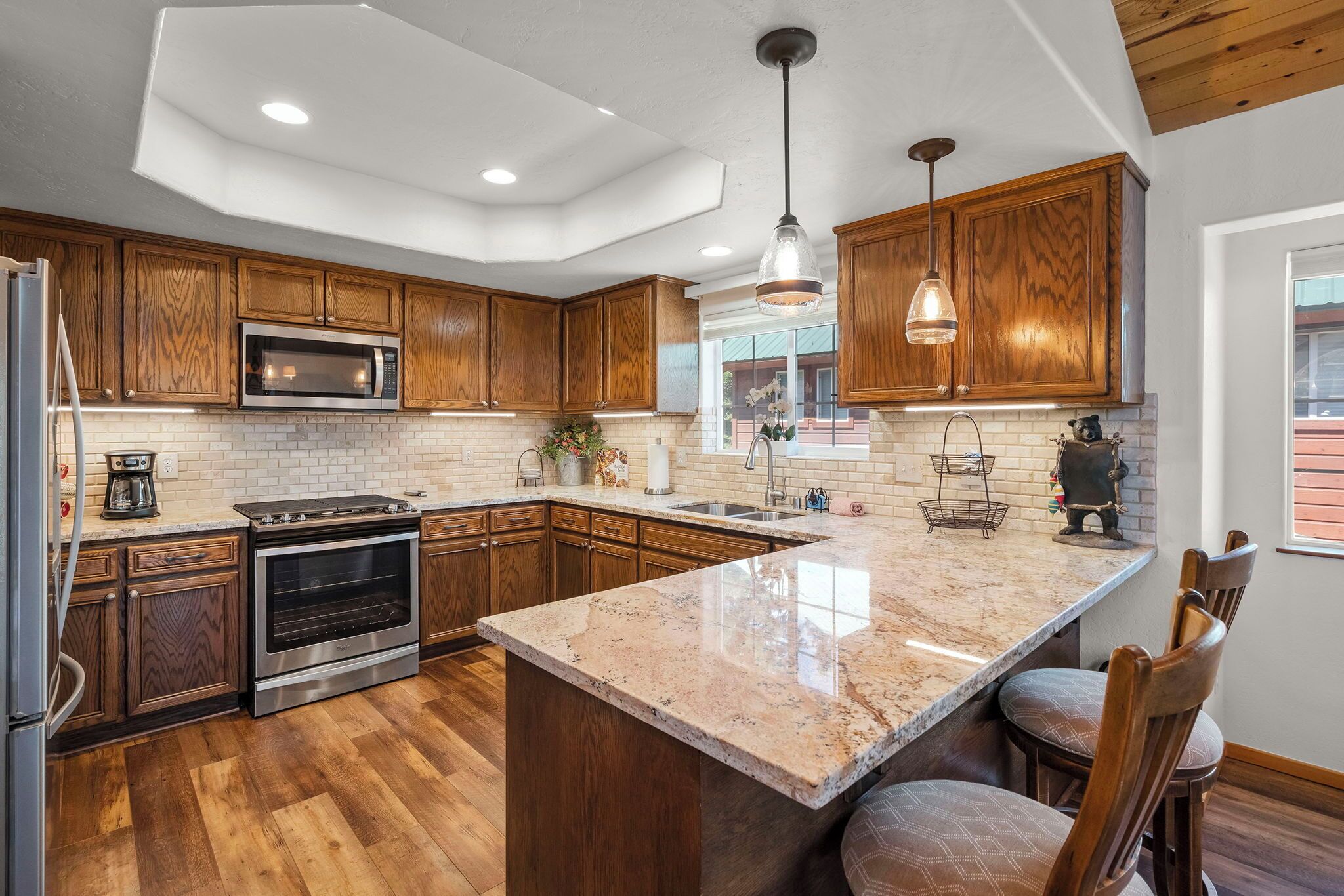 Une cuisine moderne avec des meubles en bois, un grand îlot central, des appareils en acier inoxydable et des luminaires suspendus.