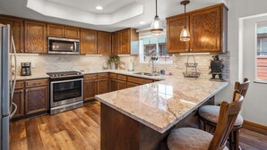 A modern kitchen with wooden cabinets, a large island, stainless steel appliances, and pendant lighting. - Pine Cone Lodge-3 bedroom, 2.5 bath home, large backyard, walk to Chambers (Tahoma)
