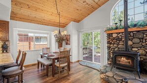 A dining area with a stone fireplace, wooden ceiling, and large windows. - Pine Cone Lodge-3 bedroom, 2.5 bath home, large backyard, walk to Chambers (Tahoma)