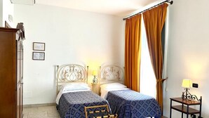 A hotel room with two beds, a wooden bench, a small table with a lamp, and a wardrobe.