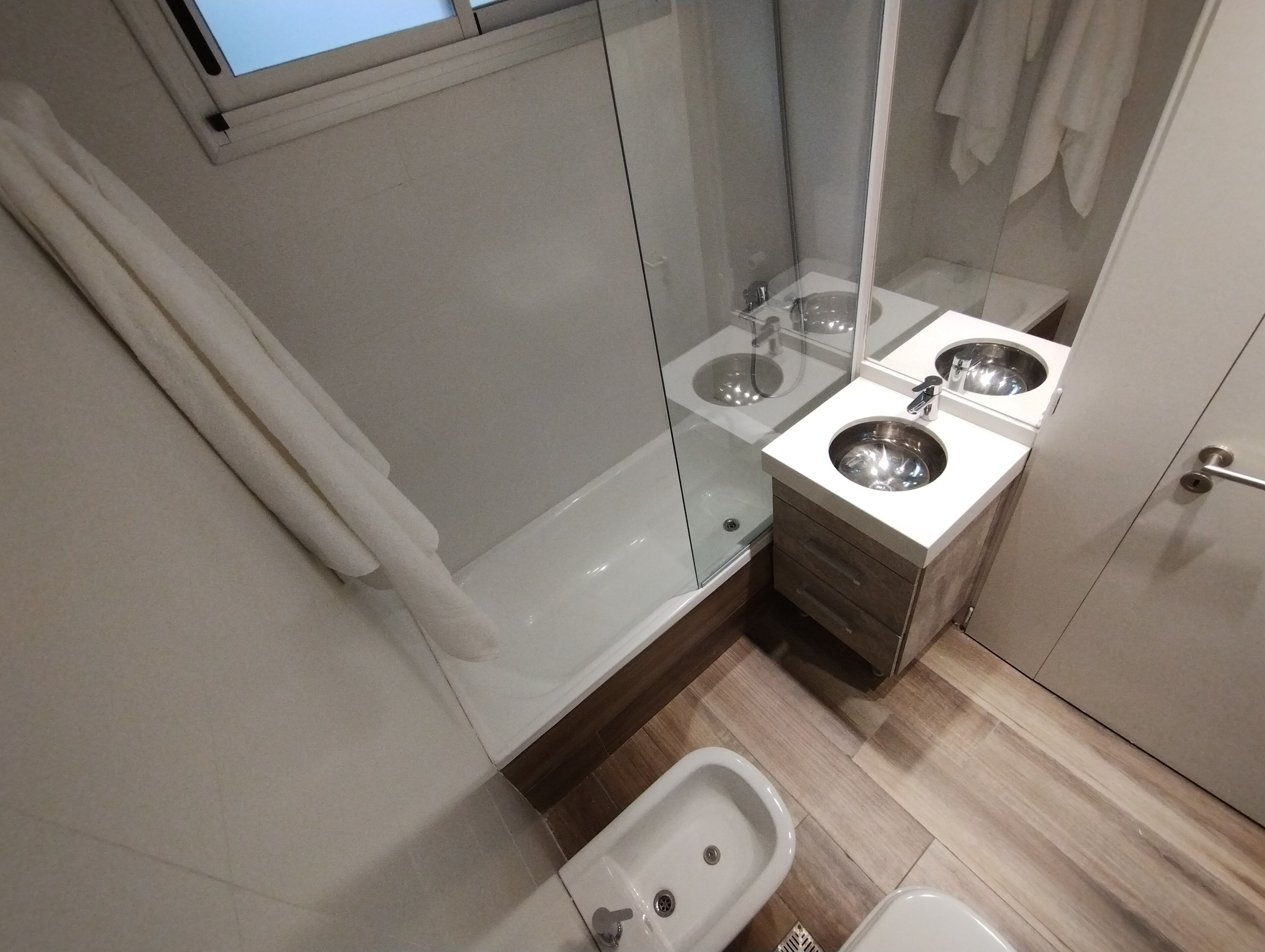 Un baño moderno con cabina de ducha de vidrio, un bidé y dos lavamanos.